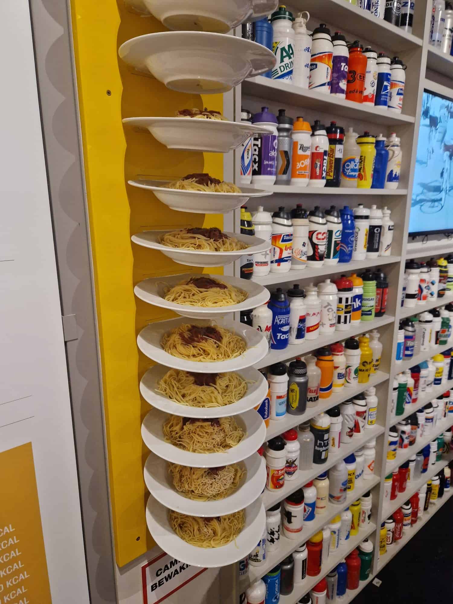 Wand vol bidons en een rij spaghettibordjes in het Centrum Ronde van Vlaanderen in Oudenaarde